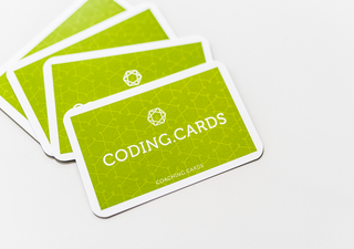 Vier Karten liegen auf hellem Untergrund. Sie zeigen die Rückseite mit dem Schriftzug Coding.Cards.