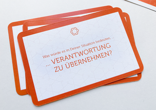 Eine Karte liegt auf einem Stapel von Karten. Auf ihr steht "Was würde es in deiner Situation bedeuten, Verantwortung zu übernehmen?"